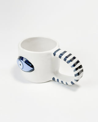 A white ceramic mug with a handcrafted blue eye design and a striped pattern on the handle on a white background.