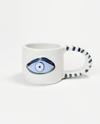 A white ceramic mug with a handcrafted blue eye design and a striped pattern on the handle on a white background.