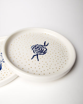 A white dessert plate with royal blue accents and gold dots, featuring a blue rose illustration in the center.