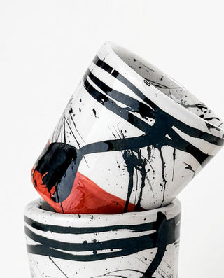 Two ceramic cups with abstract black, white, and red designs on a white background