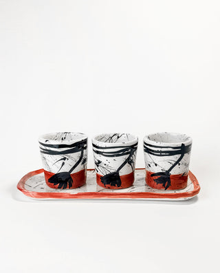 Three ceramic cups with black abstract designs on a red base, placed on a matching tray against a white background.