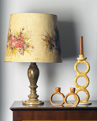 Decorative lamp with floral shade and two ceramic candle holders on a wooden surface.