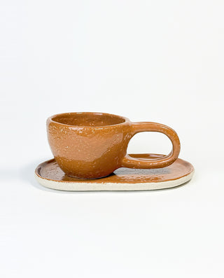 A brown ceramic mug with a caramel glaze and an oval plate, on a white background.