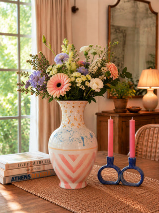 Handmade hand-painted ceramic vase with pink geometric patterns and floral arrangement on wooden table