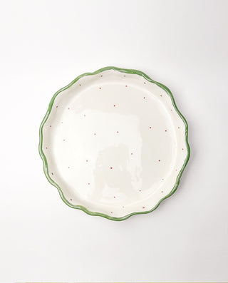 White festive ceramic plate with green rim and red speckles on a white background