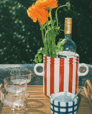 Outdoor setting with a table featuring a ceramic wine cooler, with a bottle o wine and flowers.
