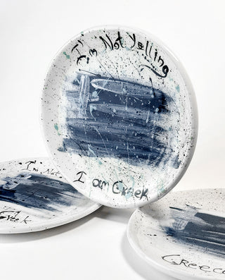 Set of white ceramic plates with black text and abstract Greek flag design on a white background