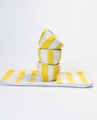 A set of three yellow and white striped espresso cups stacked together next to a matching plate with a striped pattern on a white background.