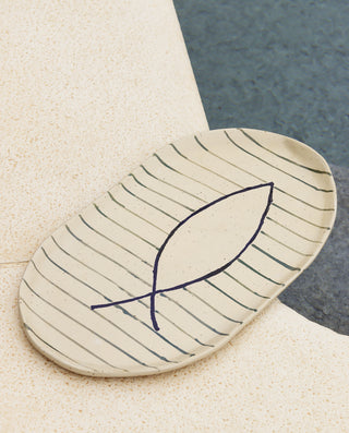 A beige oval ceramic serving platter with a striped pattern and a single fish illustration in the center.