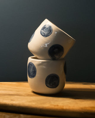 Two ceramic espresso mugs with blue polka dot design, stacked on top of each other on a wooden surface.