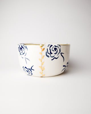 A ceramic bowl with a royal blue interior and gold details on a white exterior, featuring a floral pattern with roses.