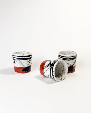 Set of five ceramic cups with black, white, and red abstract patterns on a white background