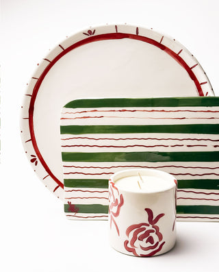 Ceramic festive platters with red and green stripes and a candle with a rose design on a white background