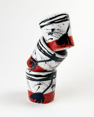 Stack of three ceramic cups with black and red abstract designs on a white background