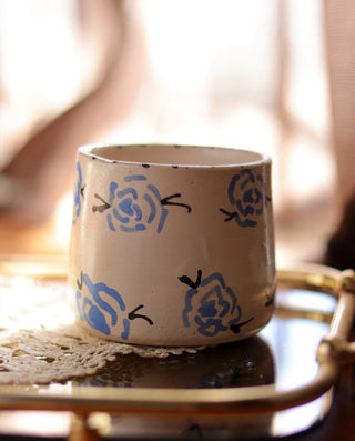 A beige ceramic mug with blue rose patterns, displayed on a table.