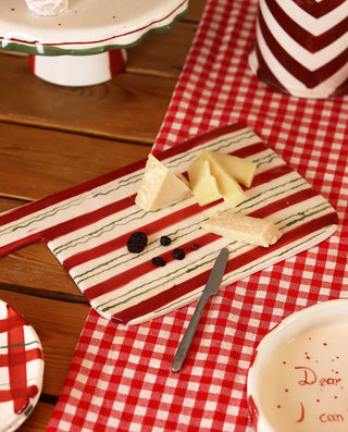 Butter on a striped cutting board with a knife on a red and white checkered tablecloth.